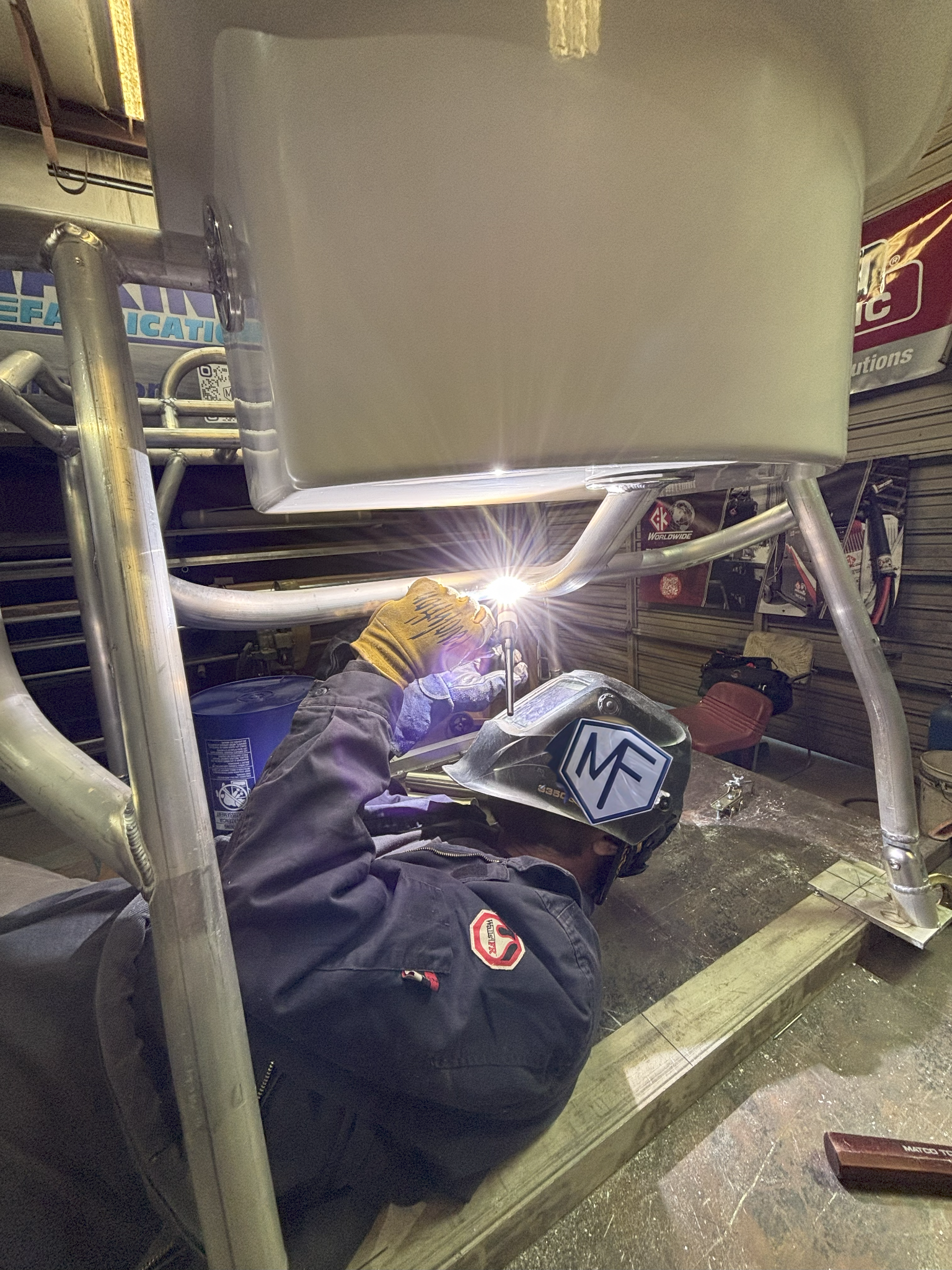 Welder in helmet welding metal chair frame in a workshop; bright light and sparks.
