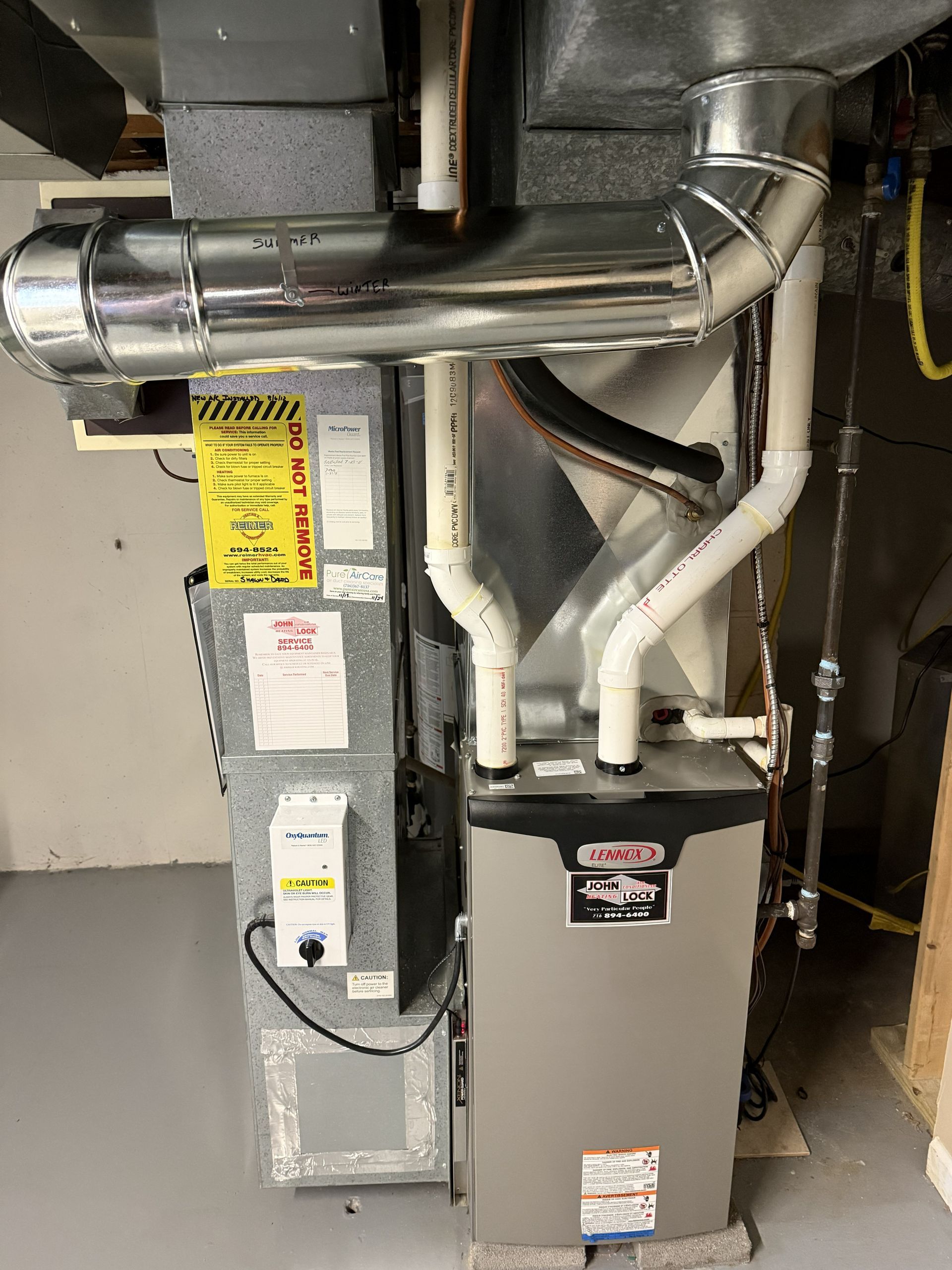 A water heater and a furnace unit standing side-by-side in a room with white walls and a concrete floor.