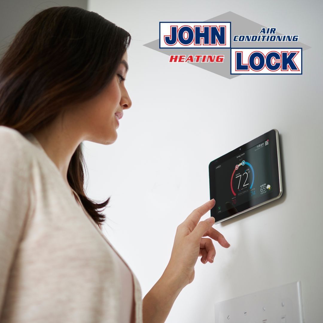 A person touches a smart home thermostat on a white wall below a John Lock Heating & Air Conditioning logo.
