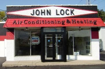 A storefront for John Lock Air Conditioning & Heating with a white, red, and black facade and a glass double door.