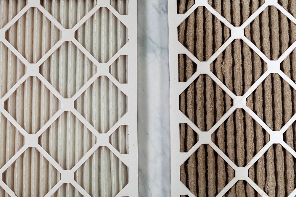 A clean white air filter sits next to a dirty, brown air filter, highlighting the difference in appearance.