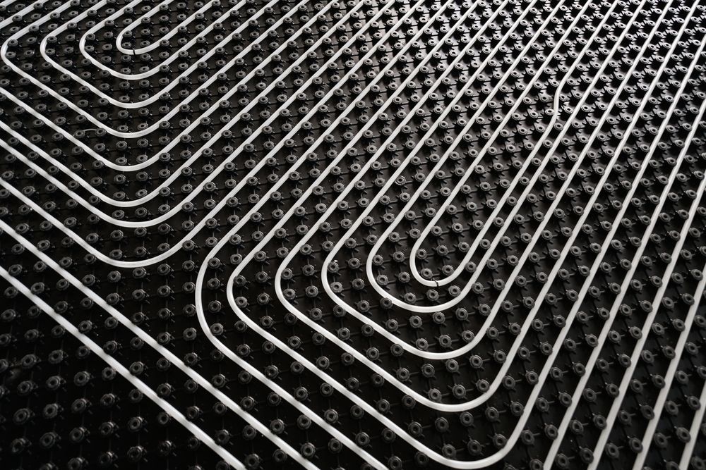 White radiant floor heating pipes installed in a snake pattern over a black dimpled insulation board.