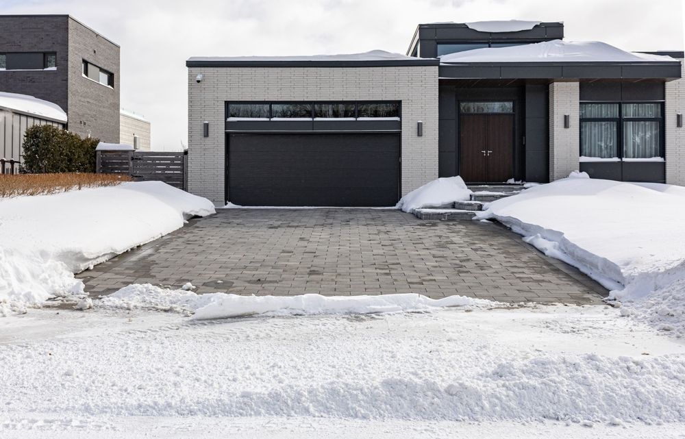 Modern house with a black garage door and paved driveway surrounded by snow on a winter day.