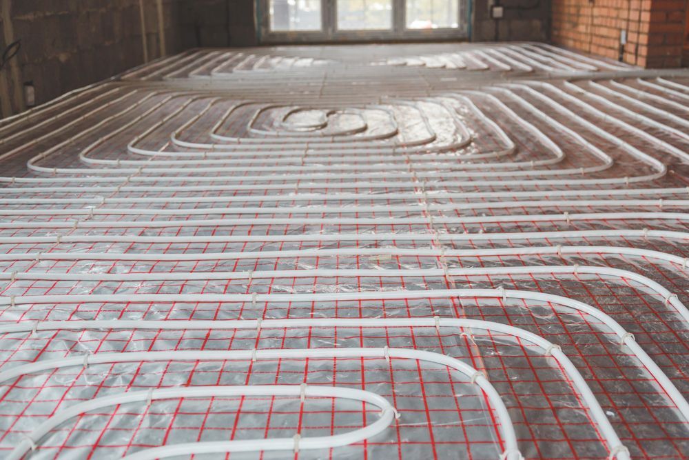 White plastic pipes arranged in a spiral pattern over a red grid on a floor during home construction.