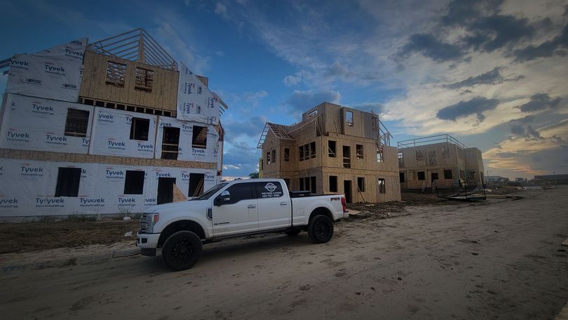 White pickup truck parked near under-construction wooden buildings, cloudy blue sky.
