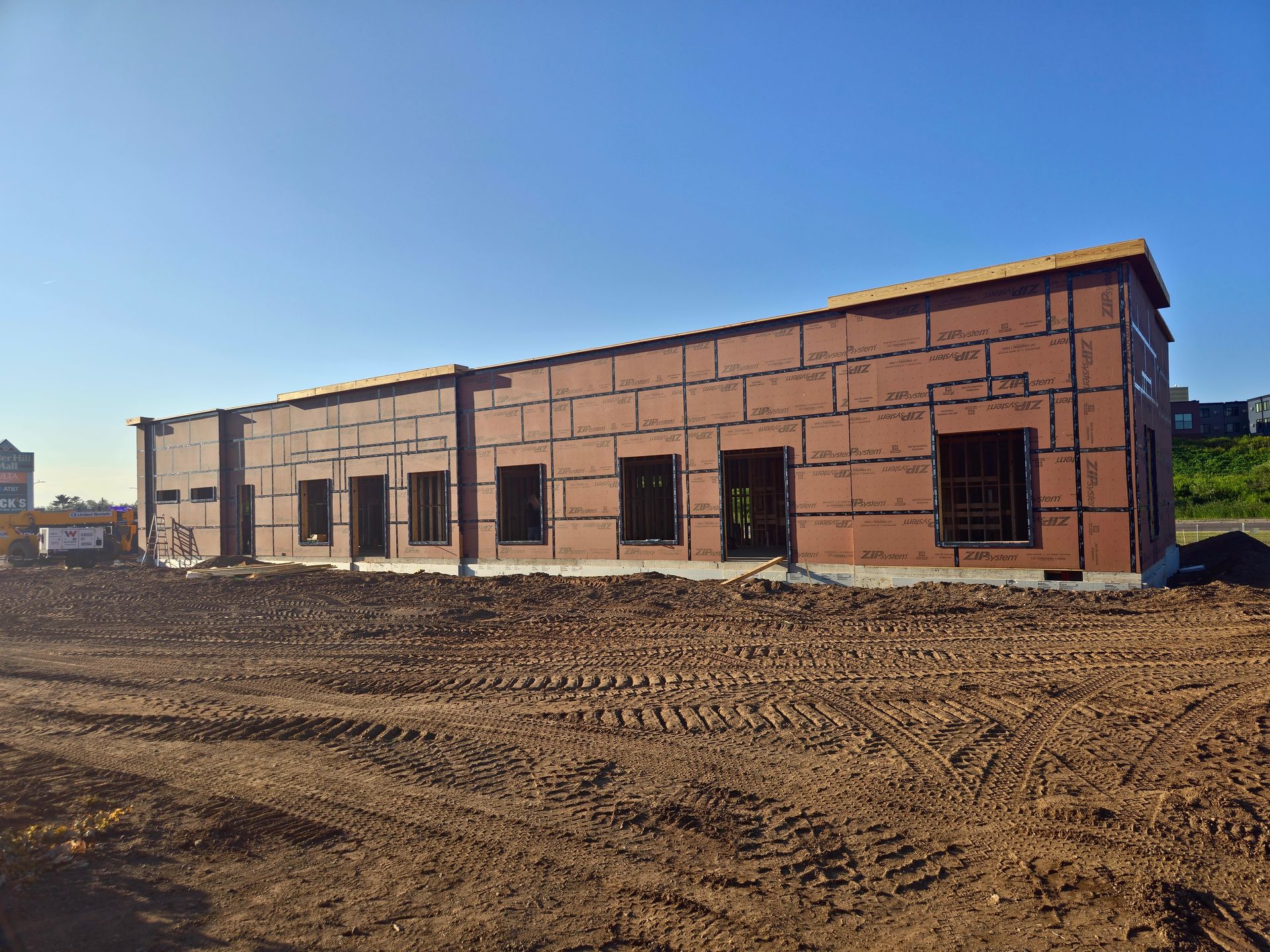 Building under construction with brown siding, several window openings, and a dirt foreground.