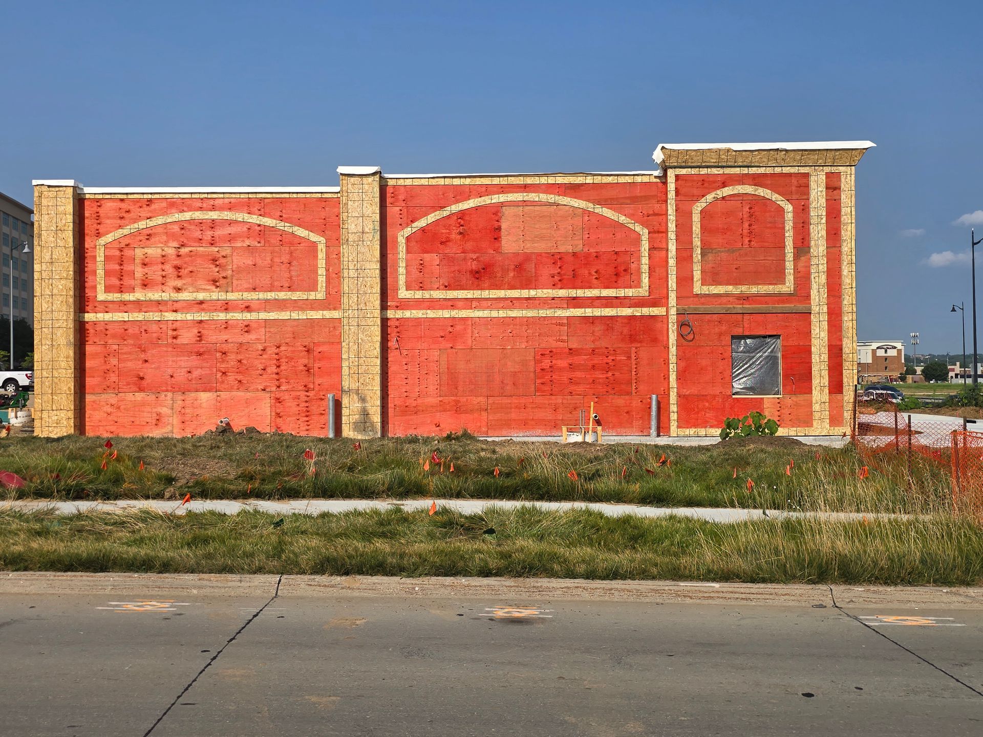 Building exterior under construction with exposed red sheathing, arched designs, and beige trim.