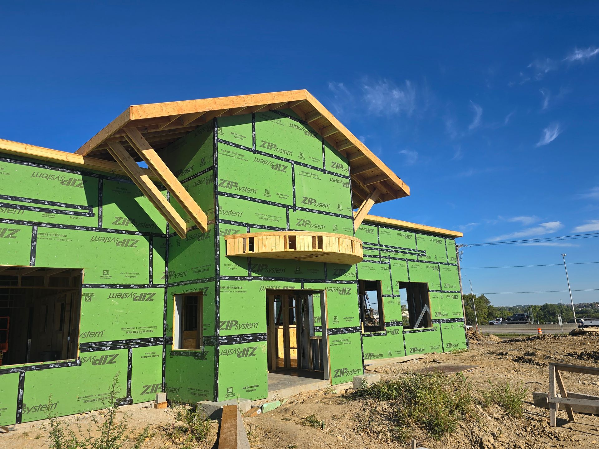 Building under construction with green insulation, exposed wood framing, and blue sky.