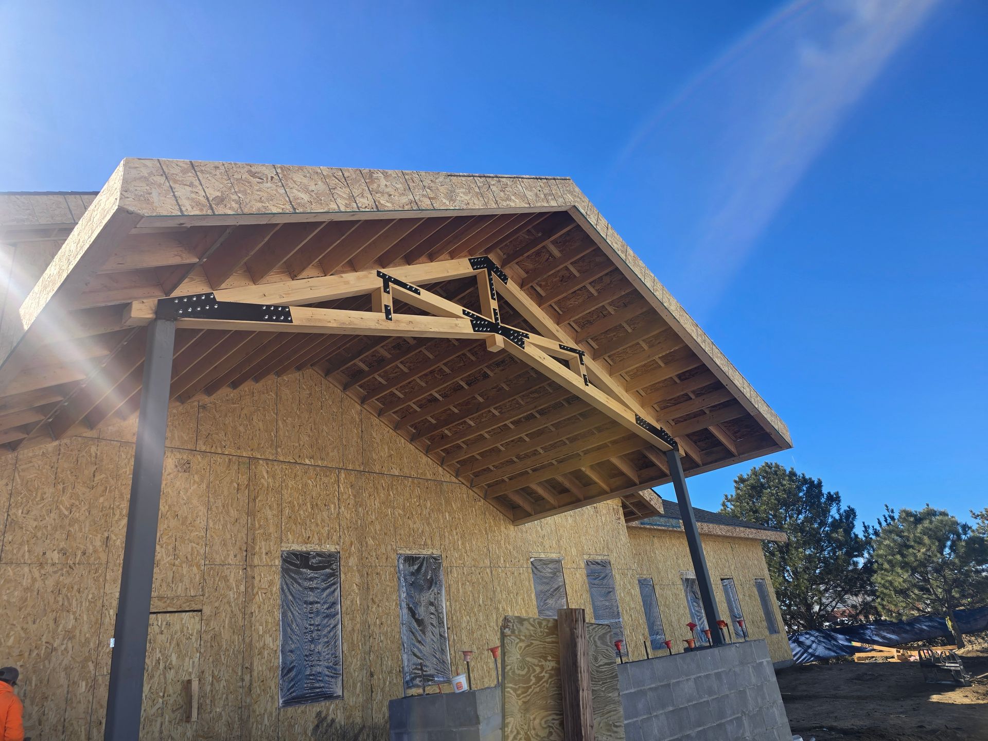 A house under construction with a roof and exposed wooden beams against a blue sky.