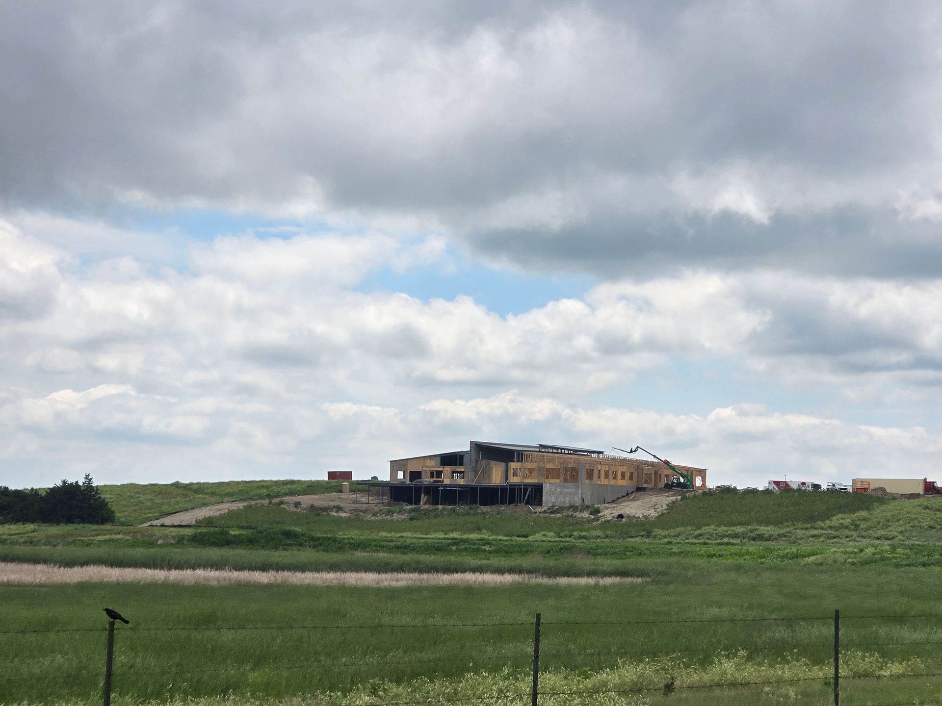 Building under construction on a grassy hill, cloudy sky.