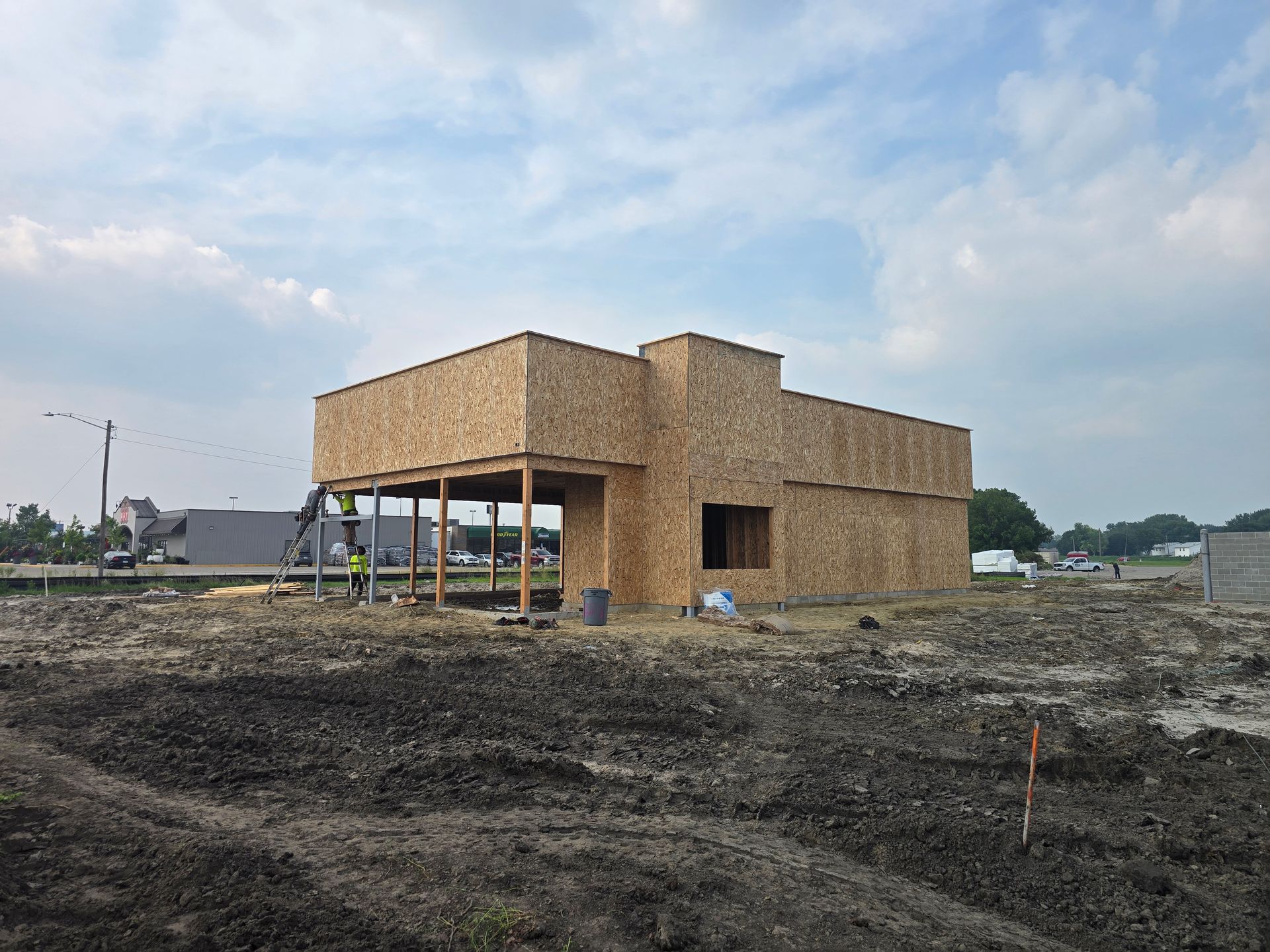Building under construction; exterior walls are wood, with open front porch. Construction site on a cloudy day.