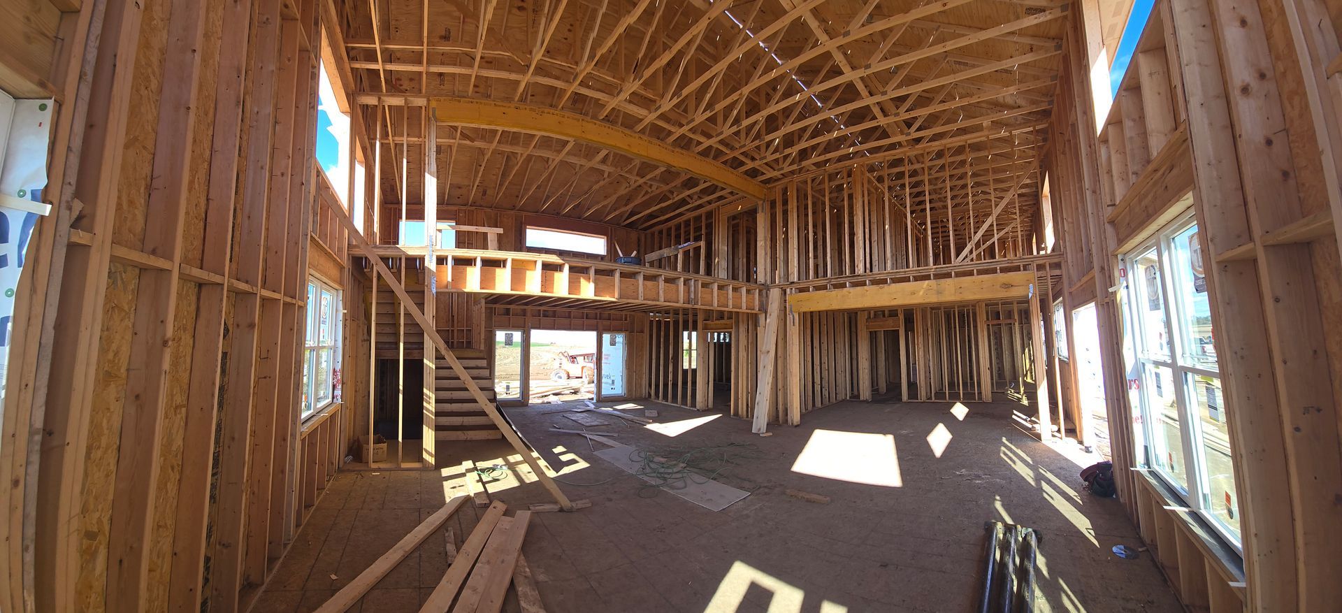 Interior view of a house under construction; wooden framing with a mezzanine, stairs, and large windows.