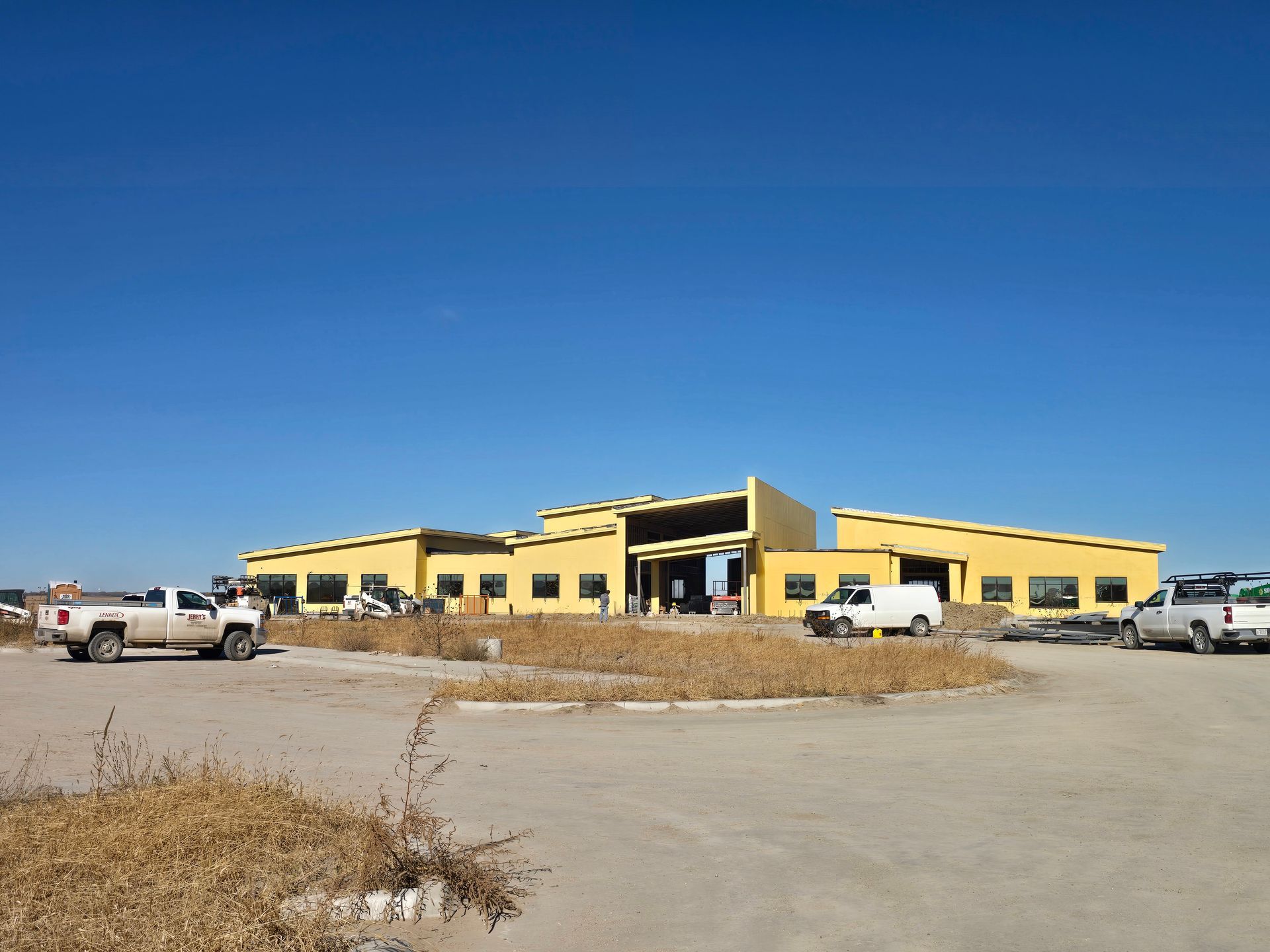 Yellow building under construction with several vehicles in the parking lot against a clear blue sky.