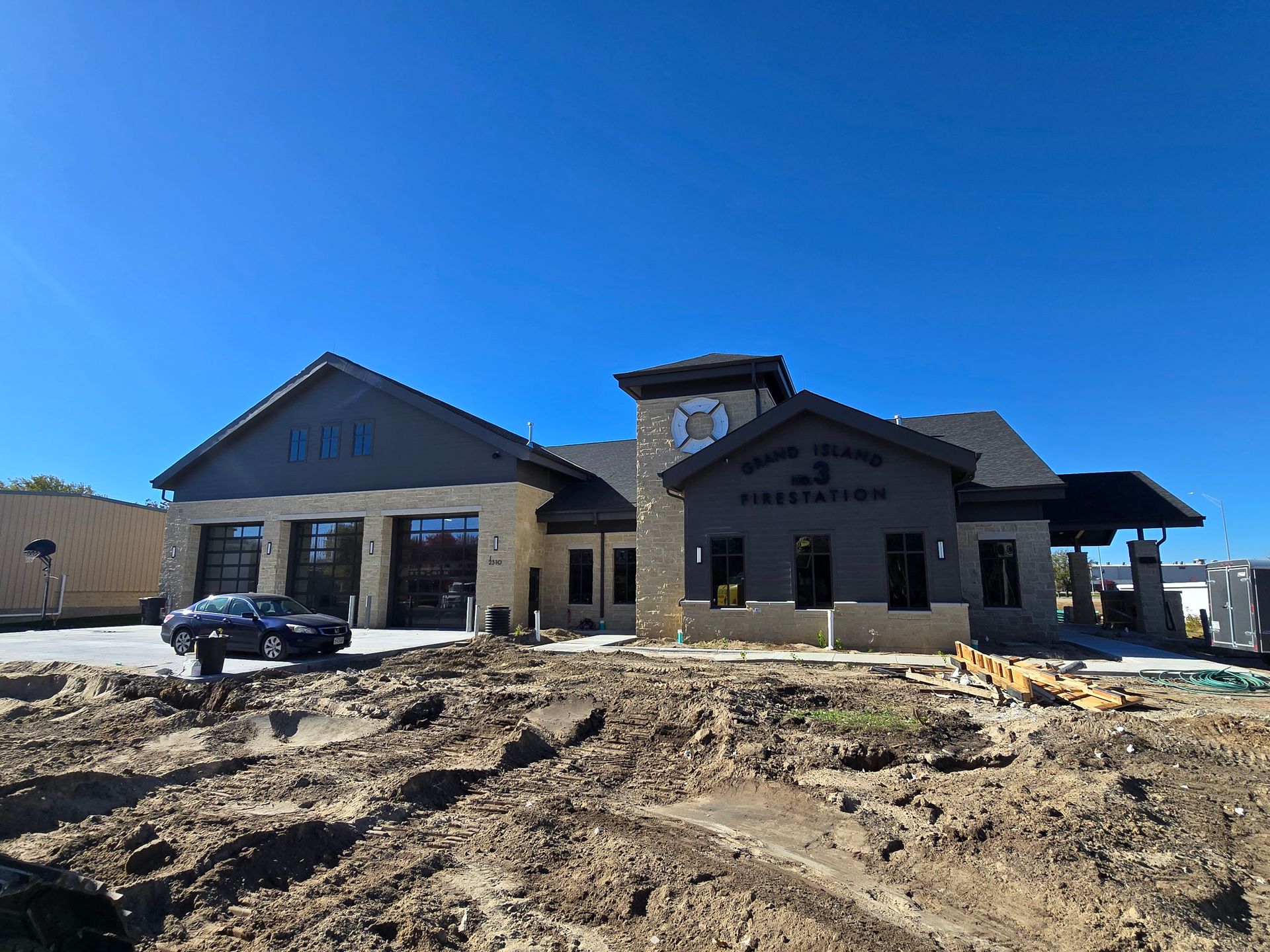 New fire station under construction on a sunny day. Building is stone and gray with black garage doors.