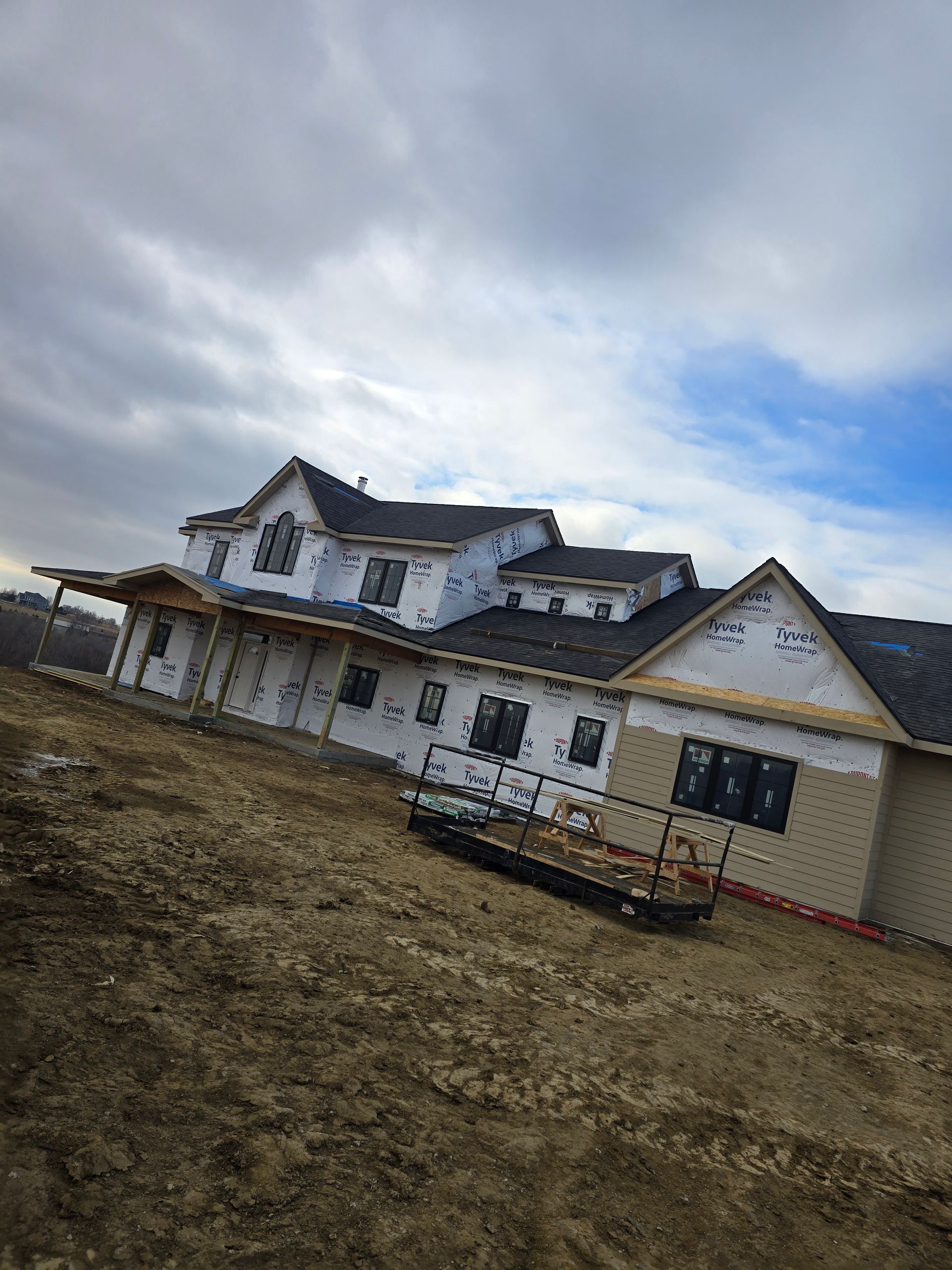 House under construction with tarpaper roof and siding on a hillside with cloudy sky.