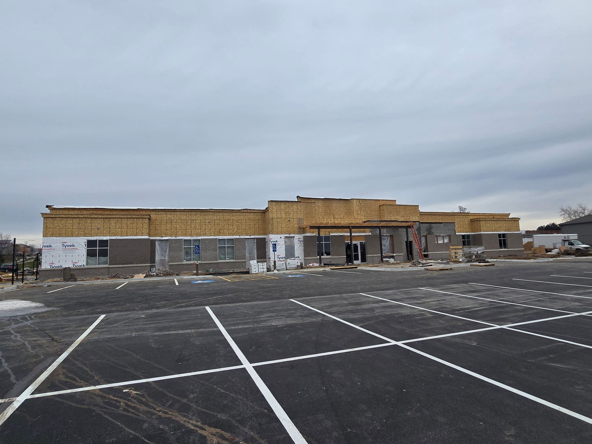 Building under construction with exposed wooden framing and empty parking lot on a cloudy day.