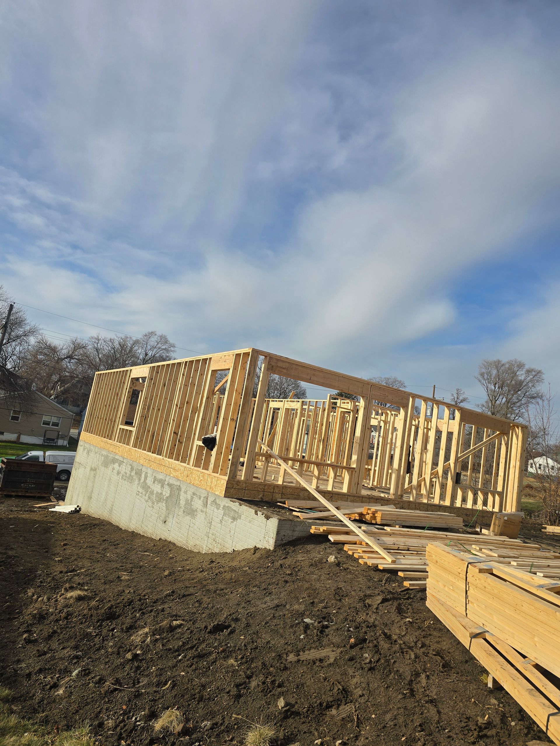 Wooden frame construction of a building on a concrete foundation, with a cloudy blue sky in the background.