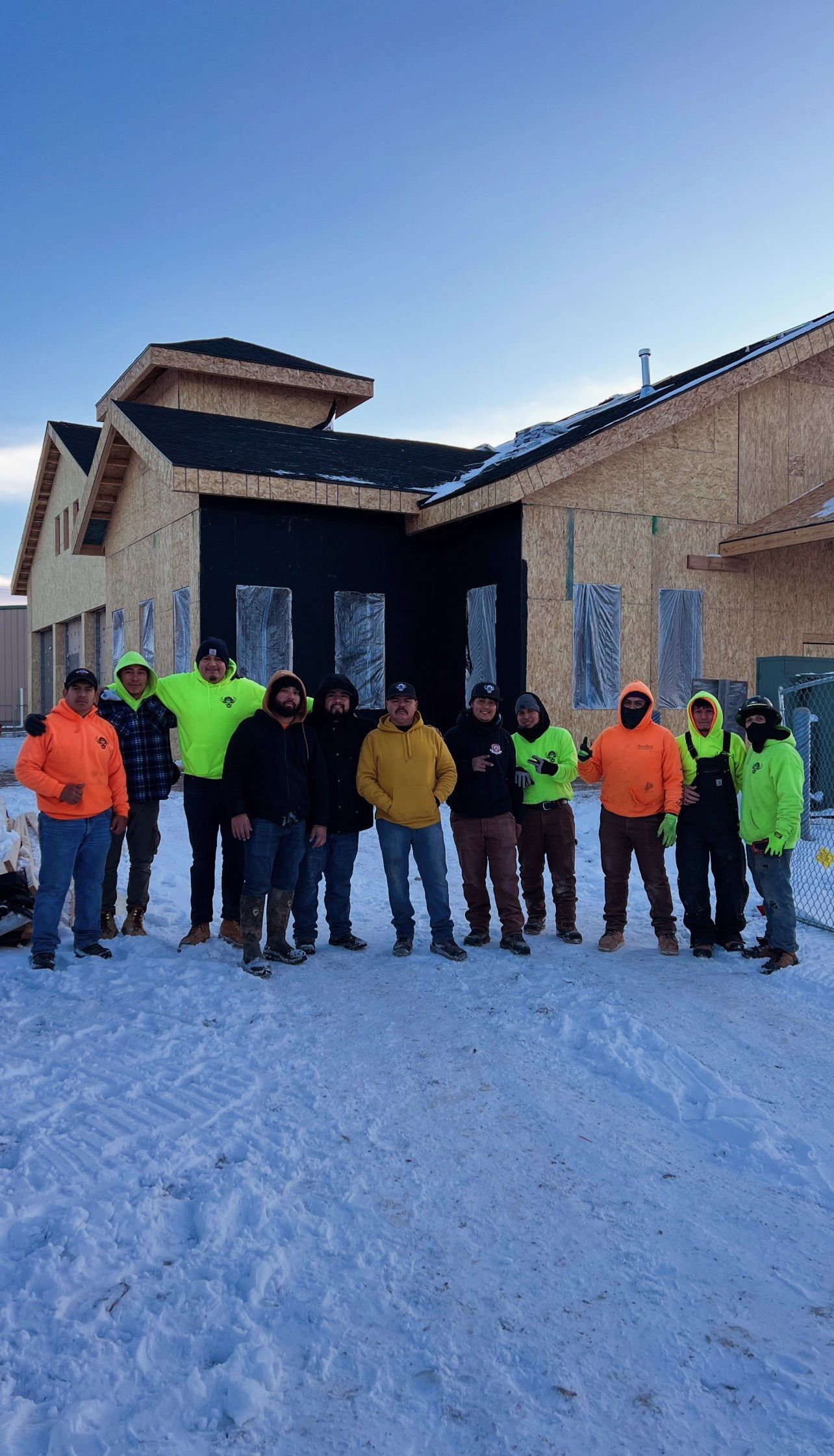 Construction crew posing in front of a building under construction, in the snow, wearing work clothes.