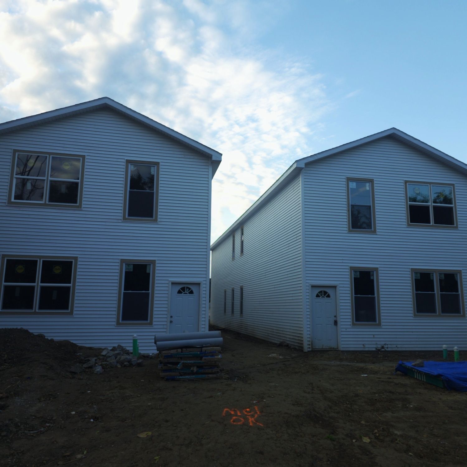 Two-story houses under construction, white siding, doors, windows, blue sky, and construction materials in the foreground.