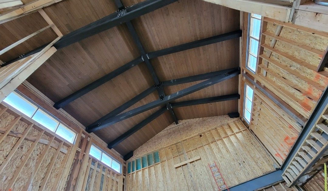 Interior view of a building under construction, showing steel beams supporting a plywood roof.