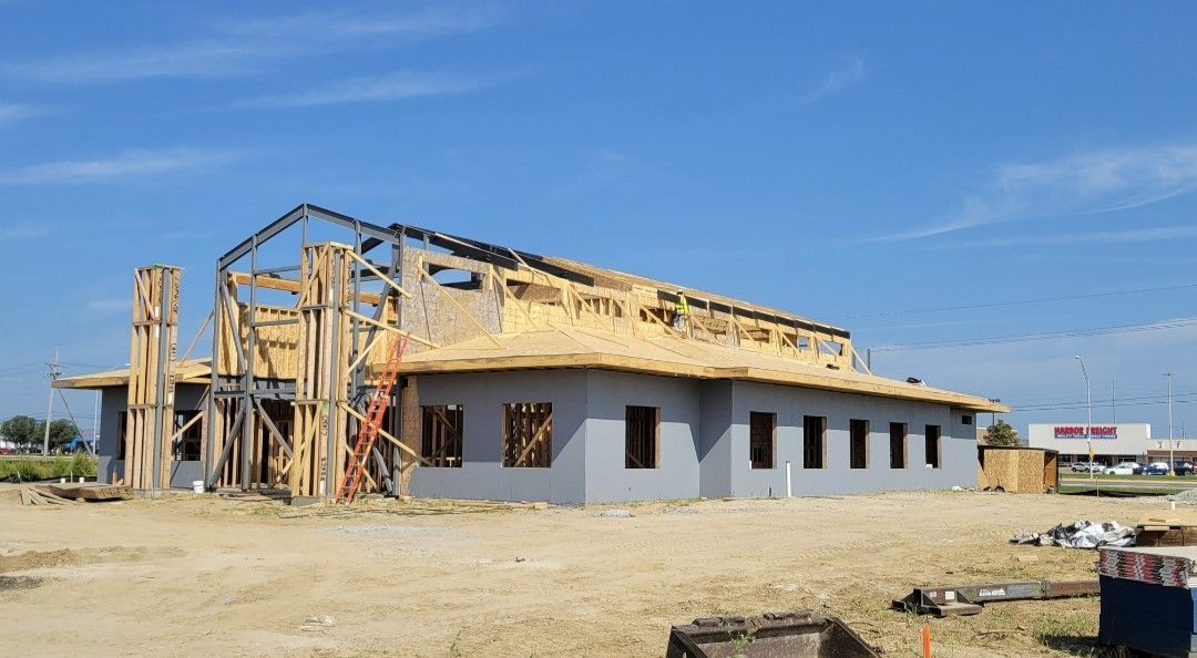 Building under construction with wooden frame, gray exterior walls, blue sky.