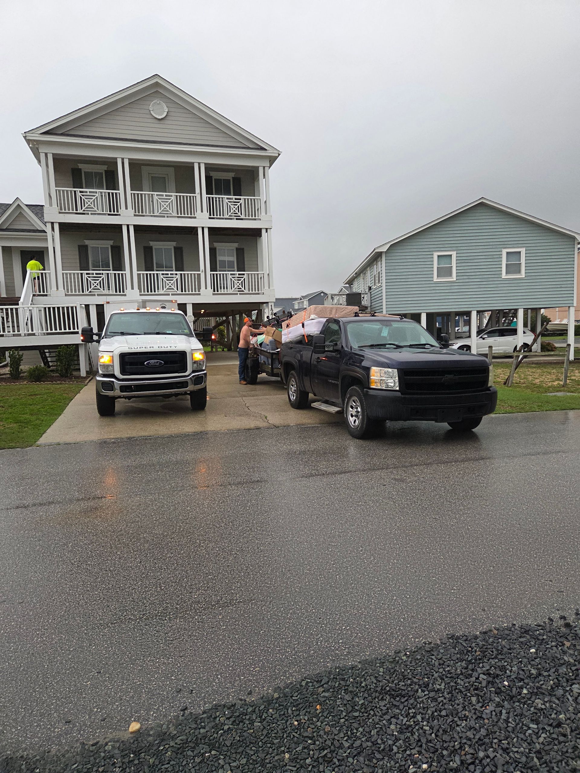 Rainy street with two pickup trucks parked before a gray house and a blue house.