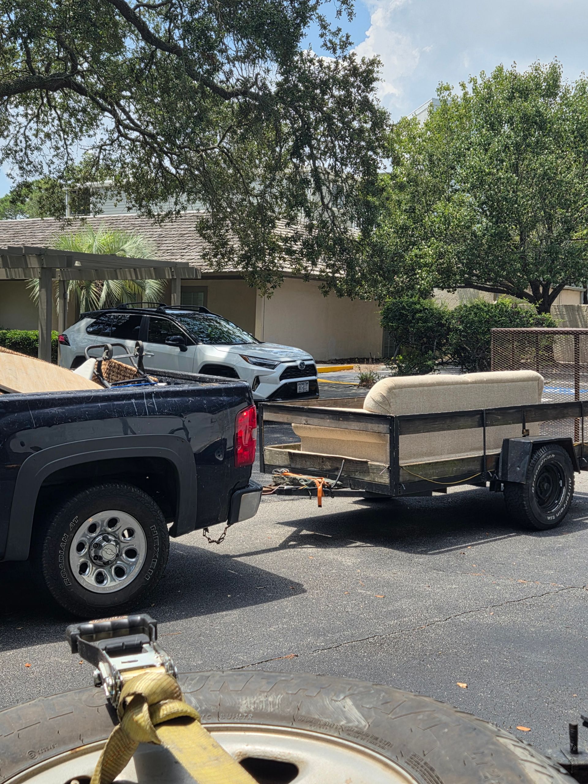 Pickup truck towing a flatbed trailer on a street with parked cars and trees nearby