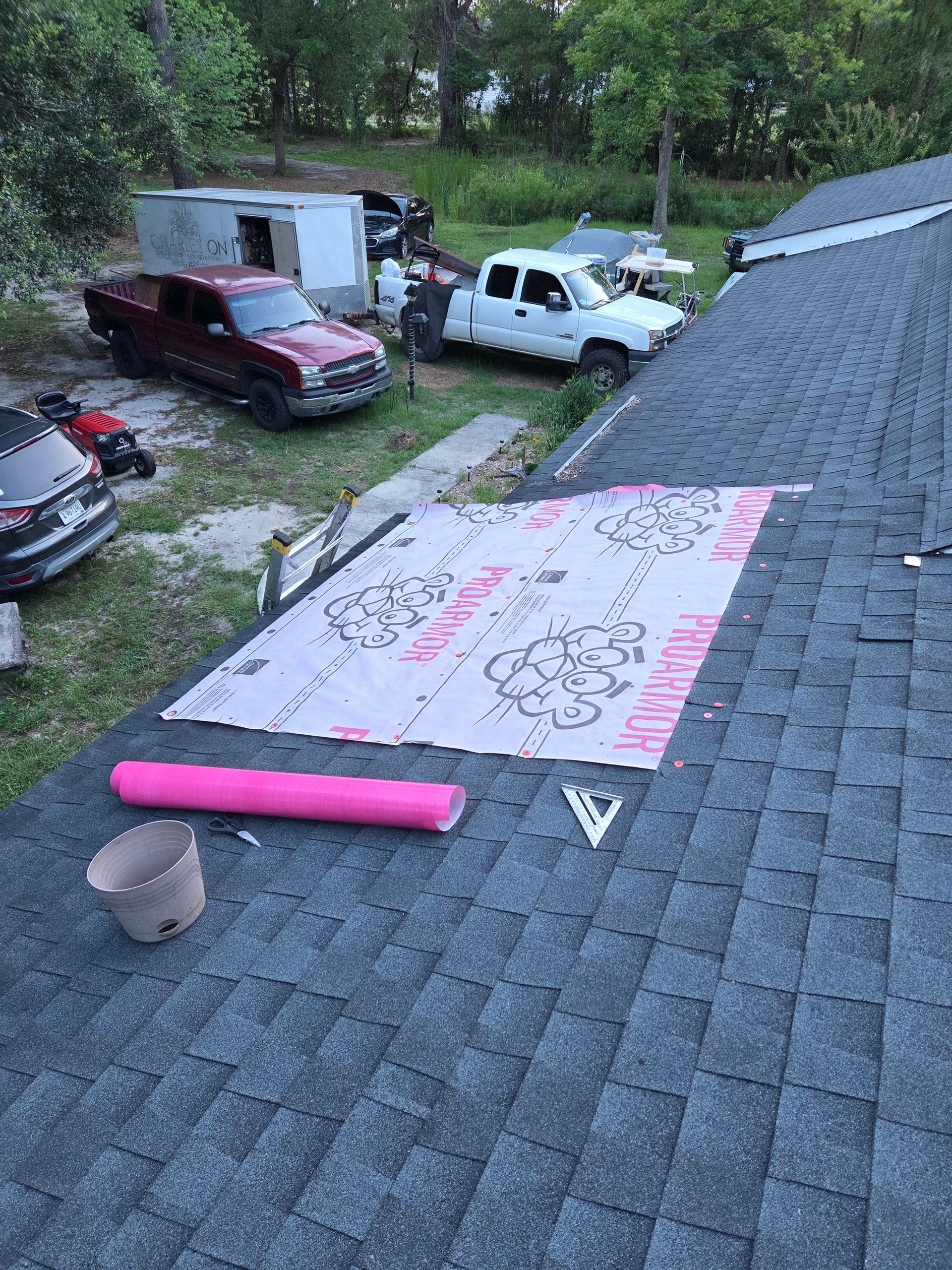 Roof with a pink banner on shingles overlooking a yard with parked cars and a trailer.