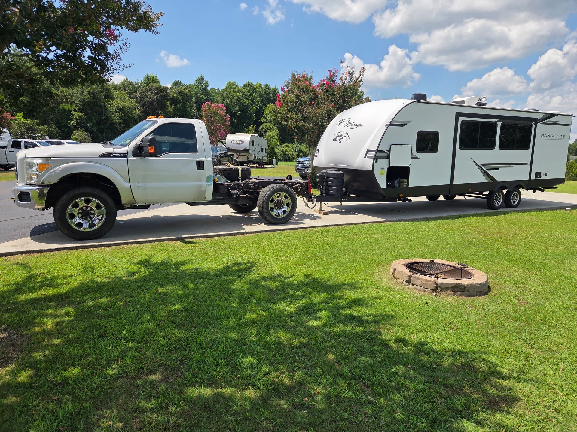 White pickup truck towing a white travel trailer on a sunny residential street with green lawn