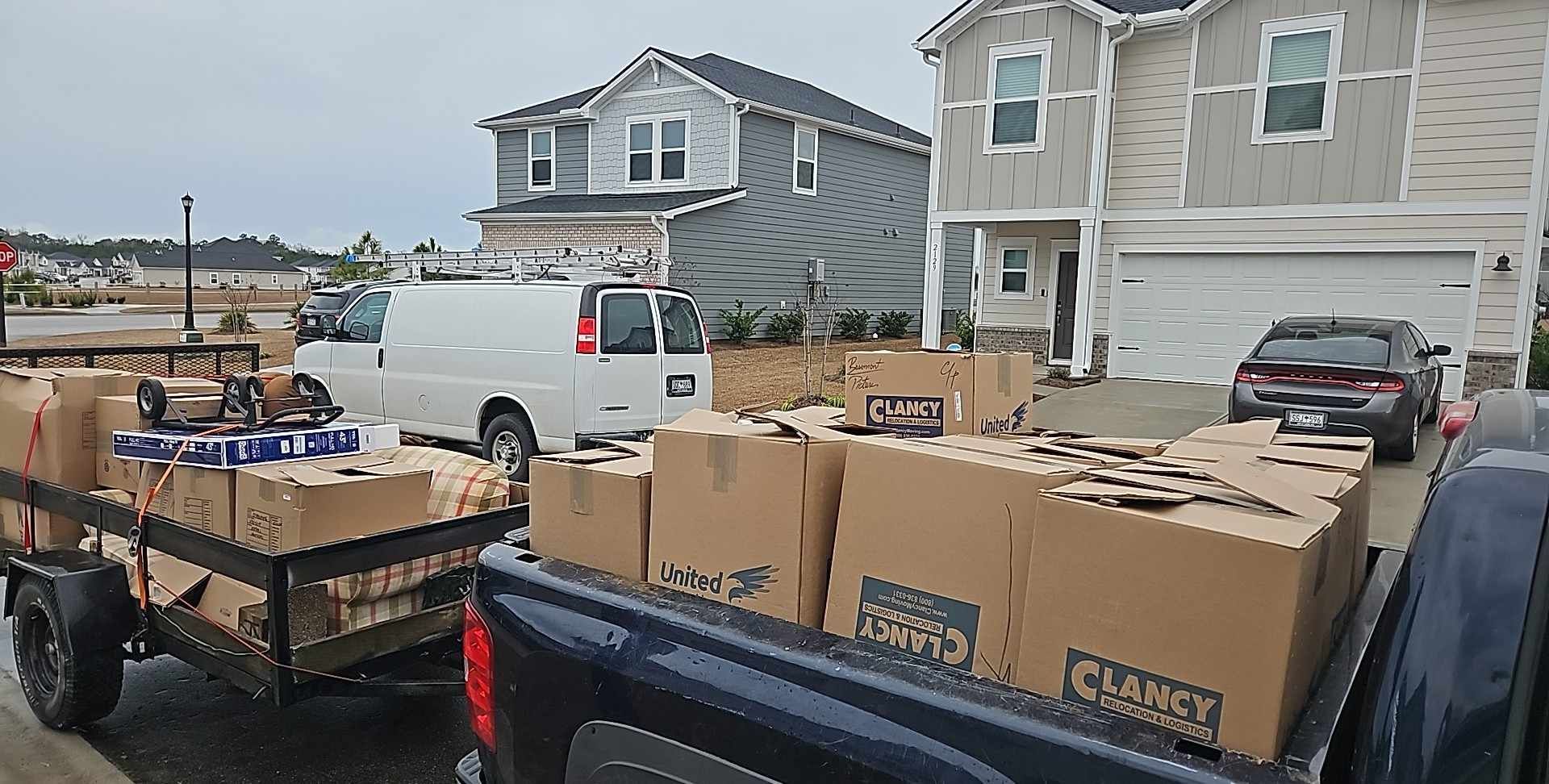 Boxes of donations loaded on trailers in a residential neighborhood, with a white van and houses nearby.