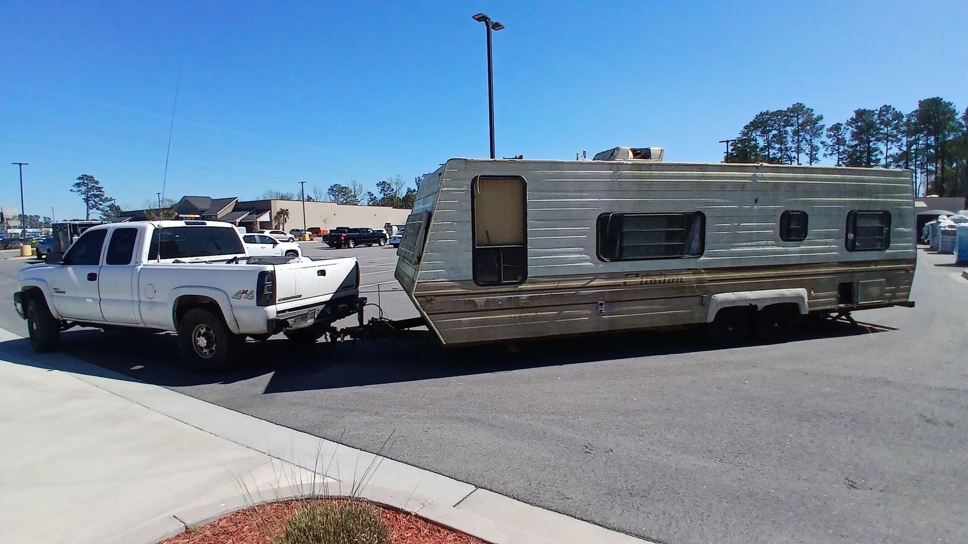 White pickup truck towing a weathered silver trailer in a parking lot on a sunny day