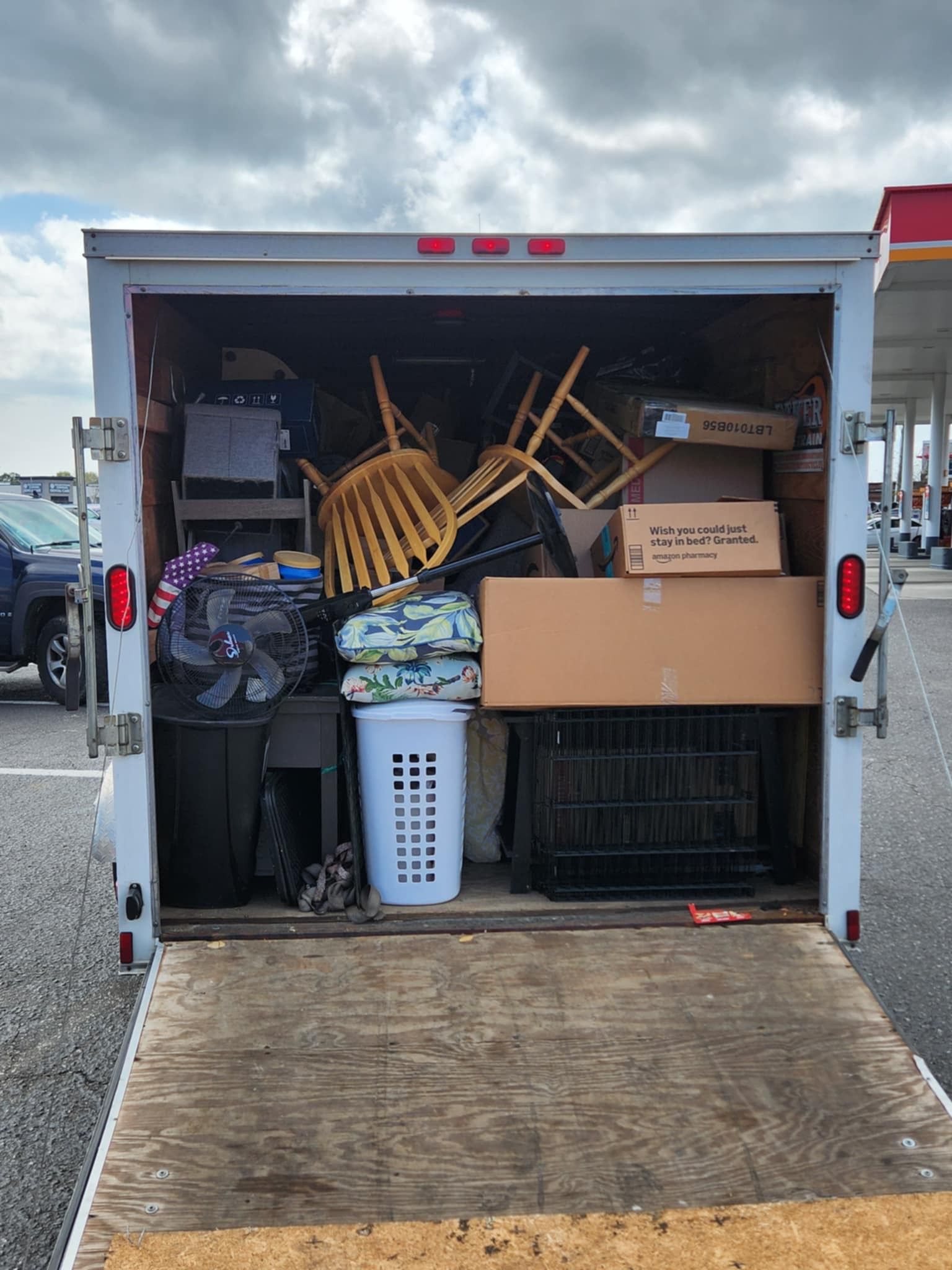 Open cargo trailer packed with chairs, boxes, and bins, with the ramp lowered.