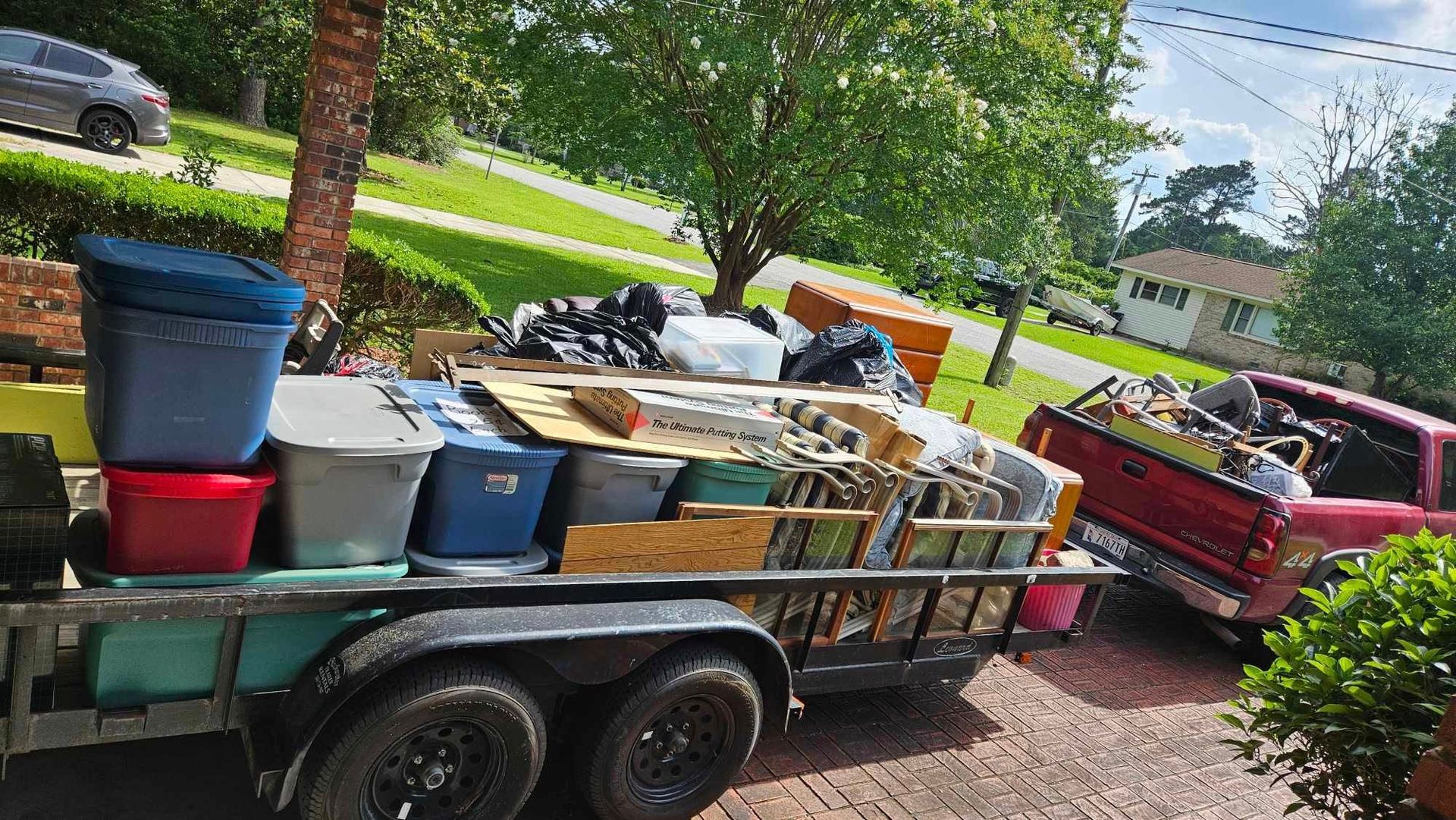 Trailer loaded with bins and yard debris beside a red pickup on a suburban street