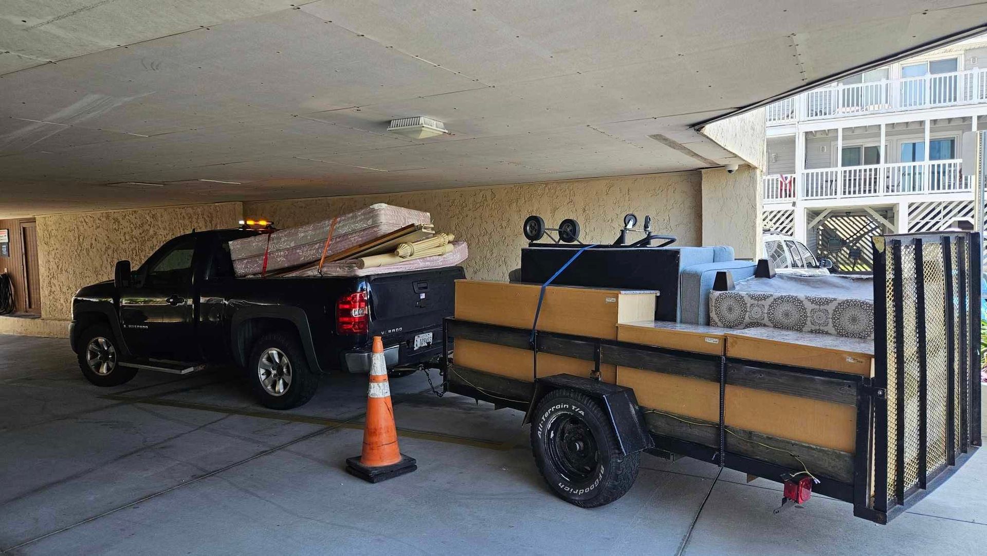 Black pickup truck towing a wood-sided trailer under a covered parking area, with an orange cone nearby