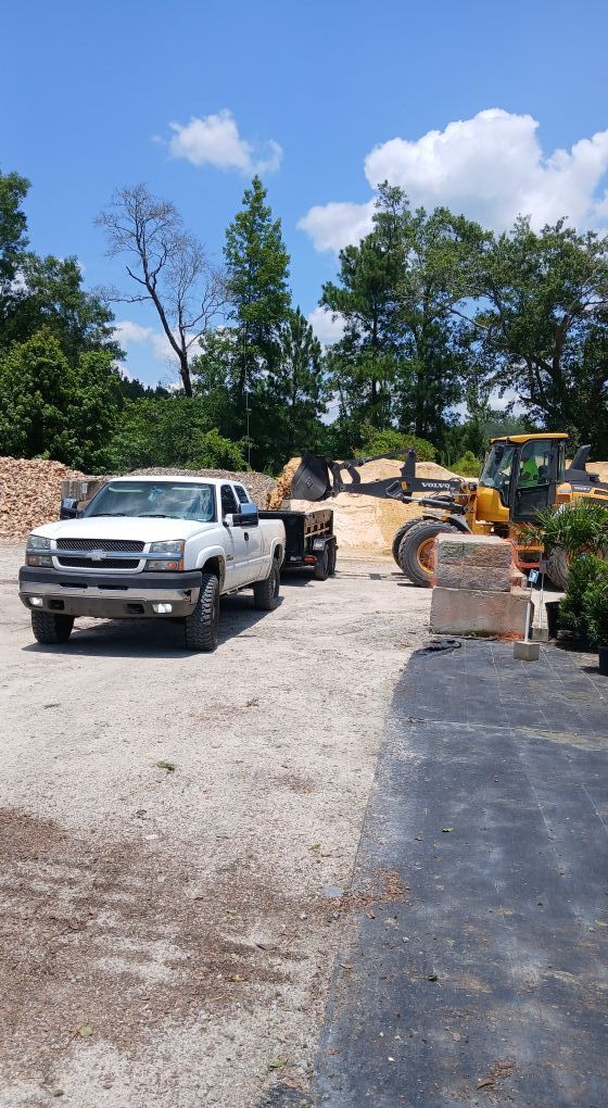 Construction worksite with pickup trucks, gravel road, and heavy equipment under a blue sky