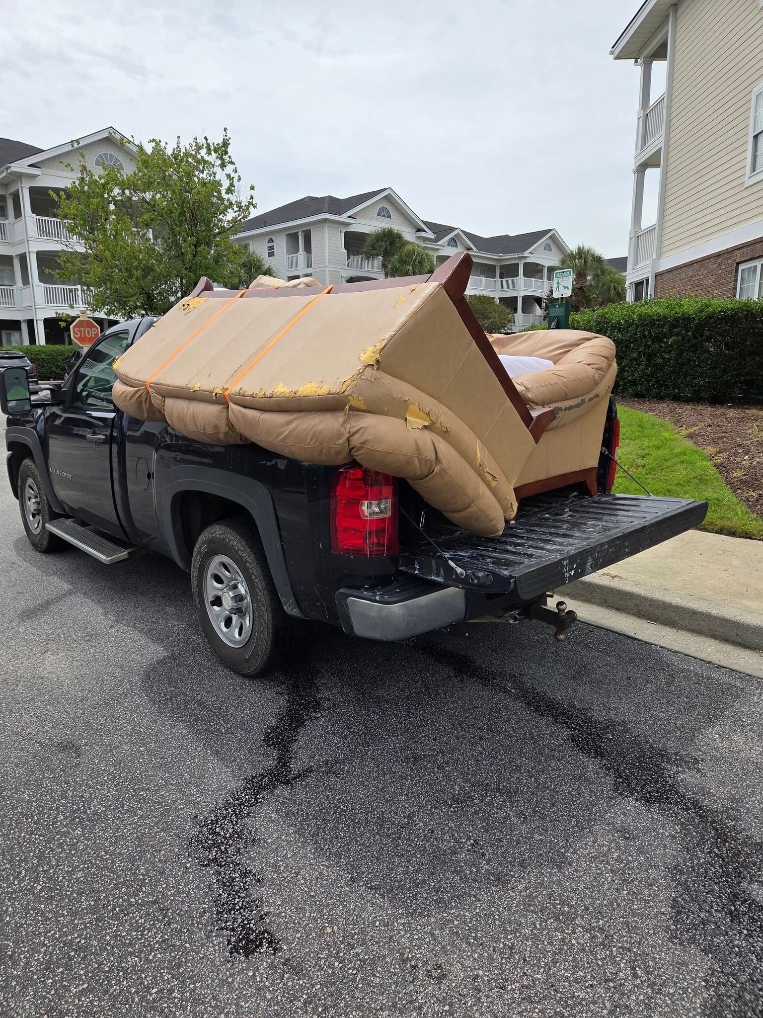 Black pickup truck parked on a wet street, loaded with a large beige couch in the bed.