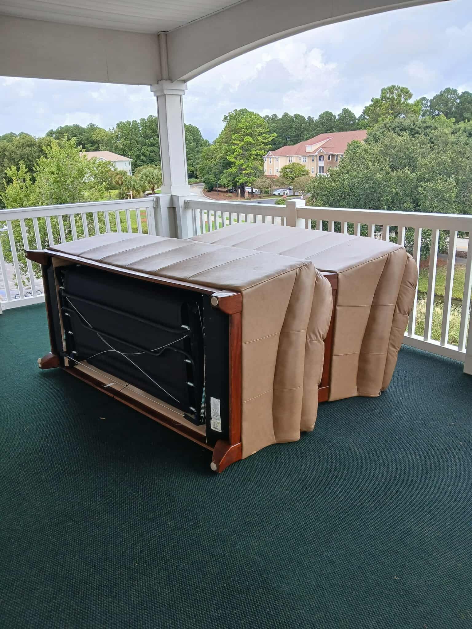 Folded wooden table lying on its side on a covered porch with white railings and green carpet.