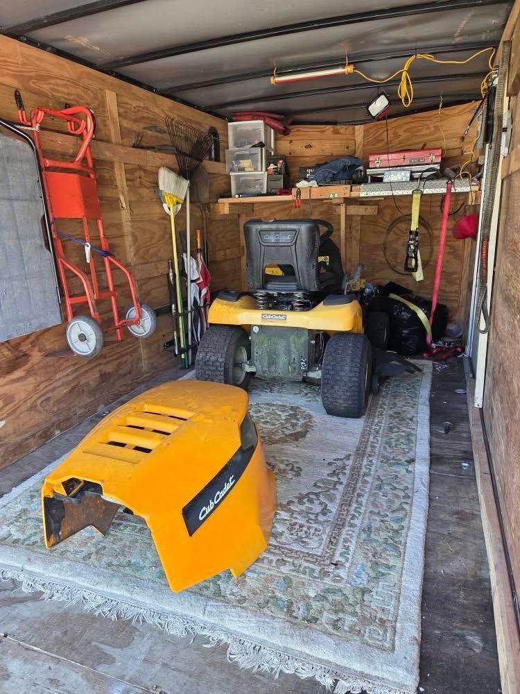 Yellow riding mower inside a cluttered garage, with a detached yellow hood in the foreground.