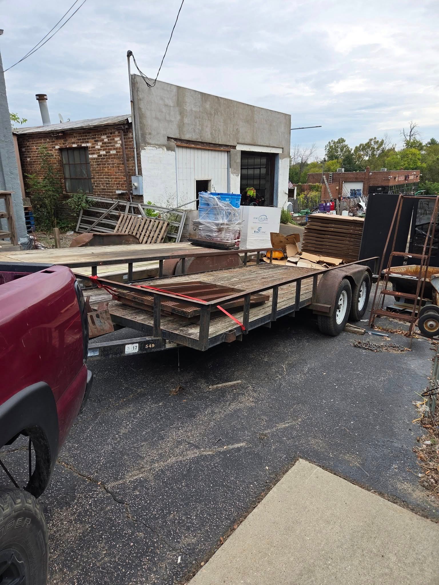 Damaged flatbed trailer loaded with debris beside a small building on a wet gravel lot