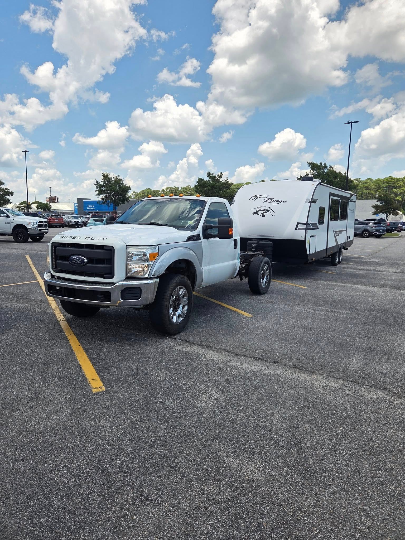 White pickup truck towing a white enclosed trailer in a parking lot under a partly cloudy sky