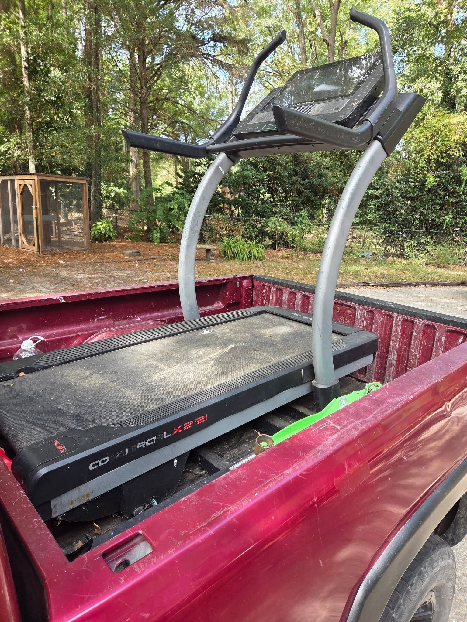 Treadmill secured in the bed of a red pickup truck under a wooded outdoor setting