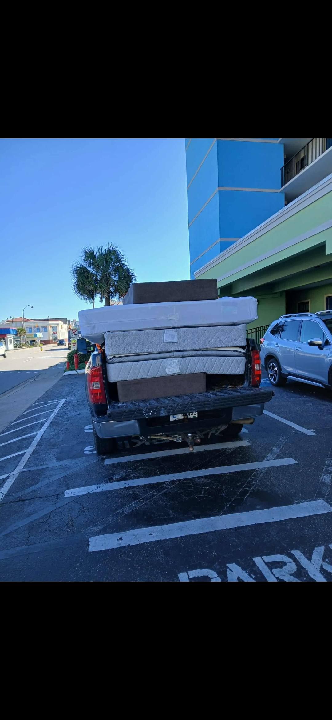 Pickup truck loaded with stacked boards parked outside a building under a clear blue sky