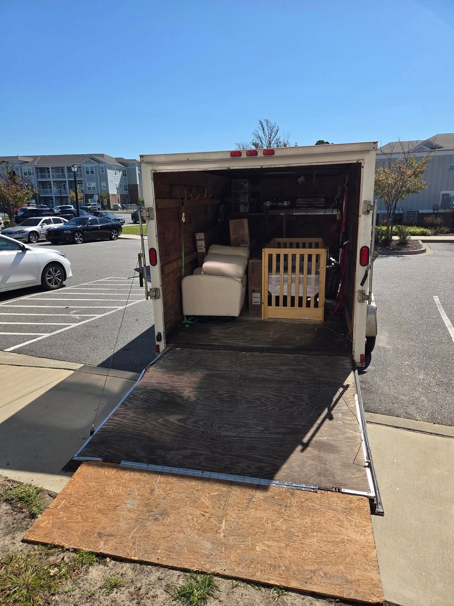 Open box truck with ramp lowered in a parking lot, showing furniture and equipment inside.