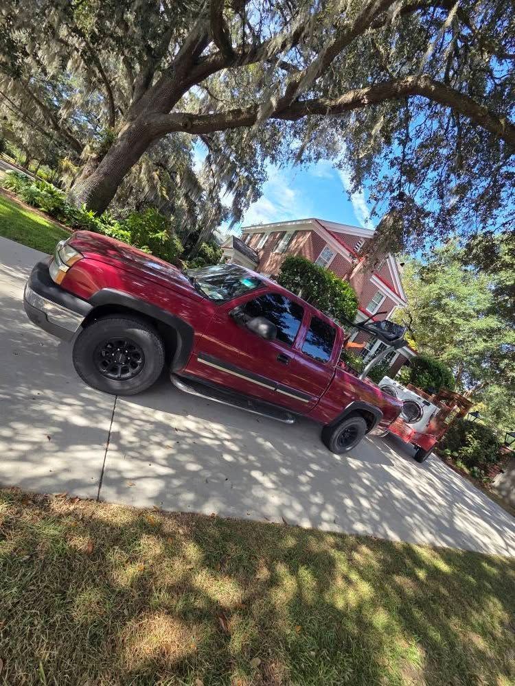 Red lifted pickup truck parked on a tree-lined residential street near a pink house.