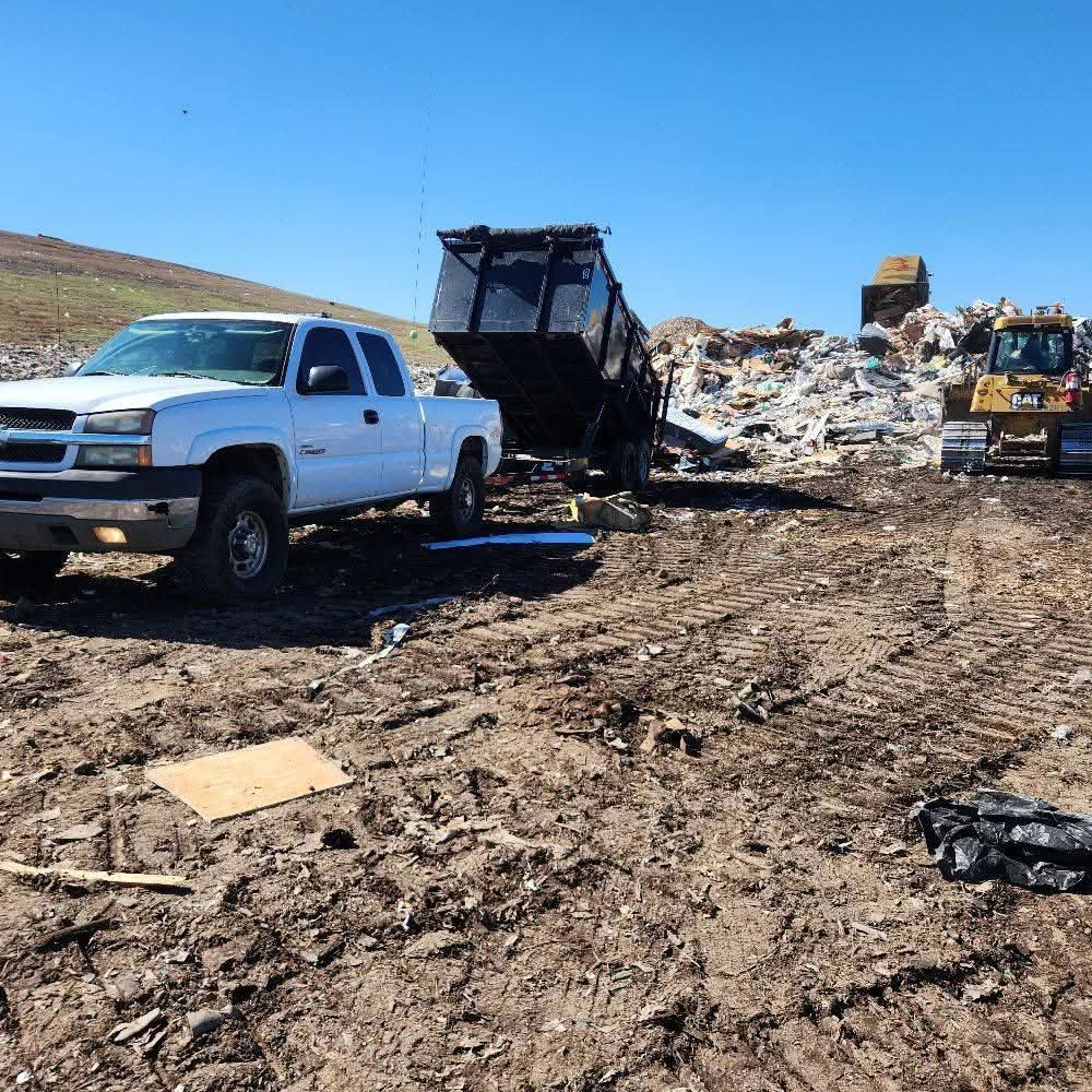 White pickup truck near a dump truck at a muddy landfill under a clear blue sky