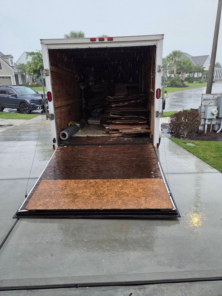 Open box truck with lowered ramp on a rainy driveway, showing stacked wood inside.
