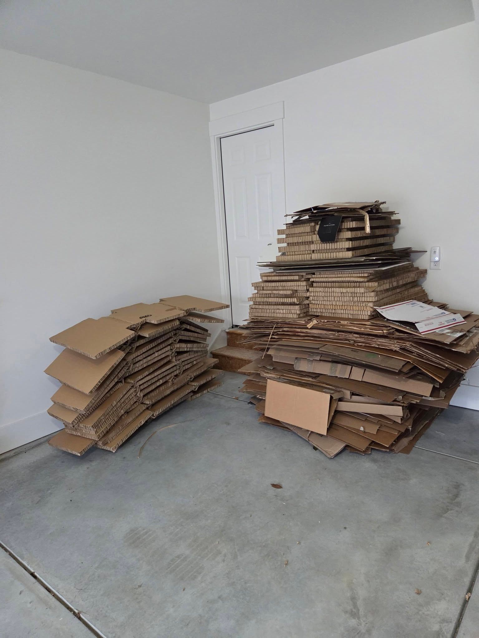 Stacks of flattened cardboard boxes piled in a bare room with a concrete floor.