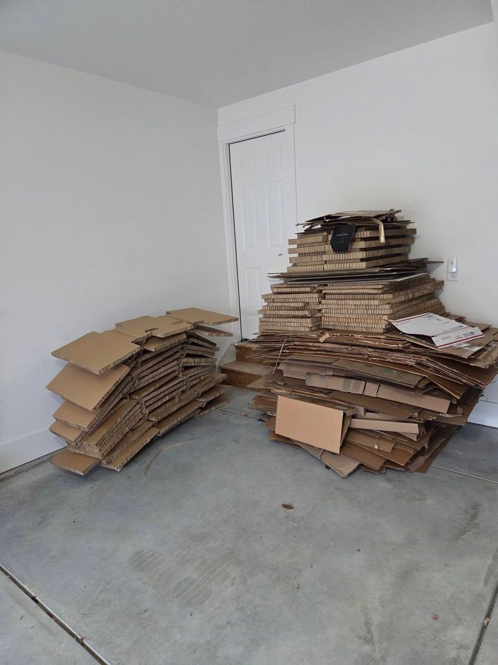 Stacks of flattened cardboard boxes piled in a bare room with a concrete floor.