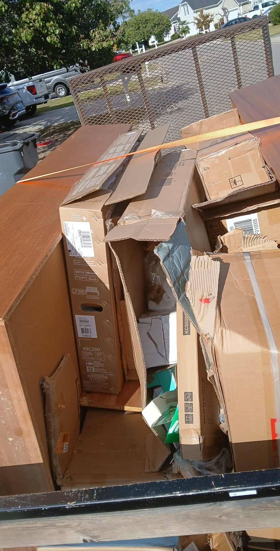 Pile of large cardboard boxes and packing materials stacked in an open truck bed outdoors