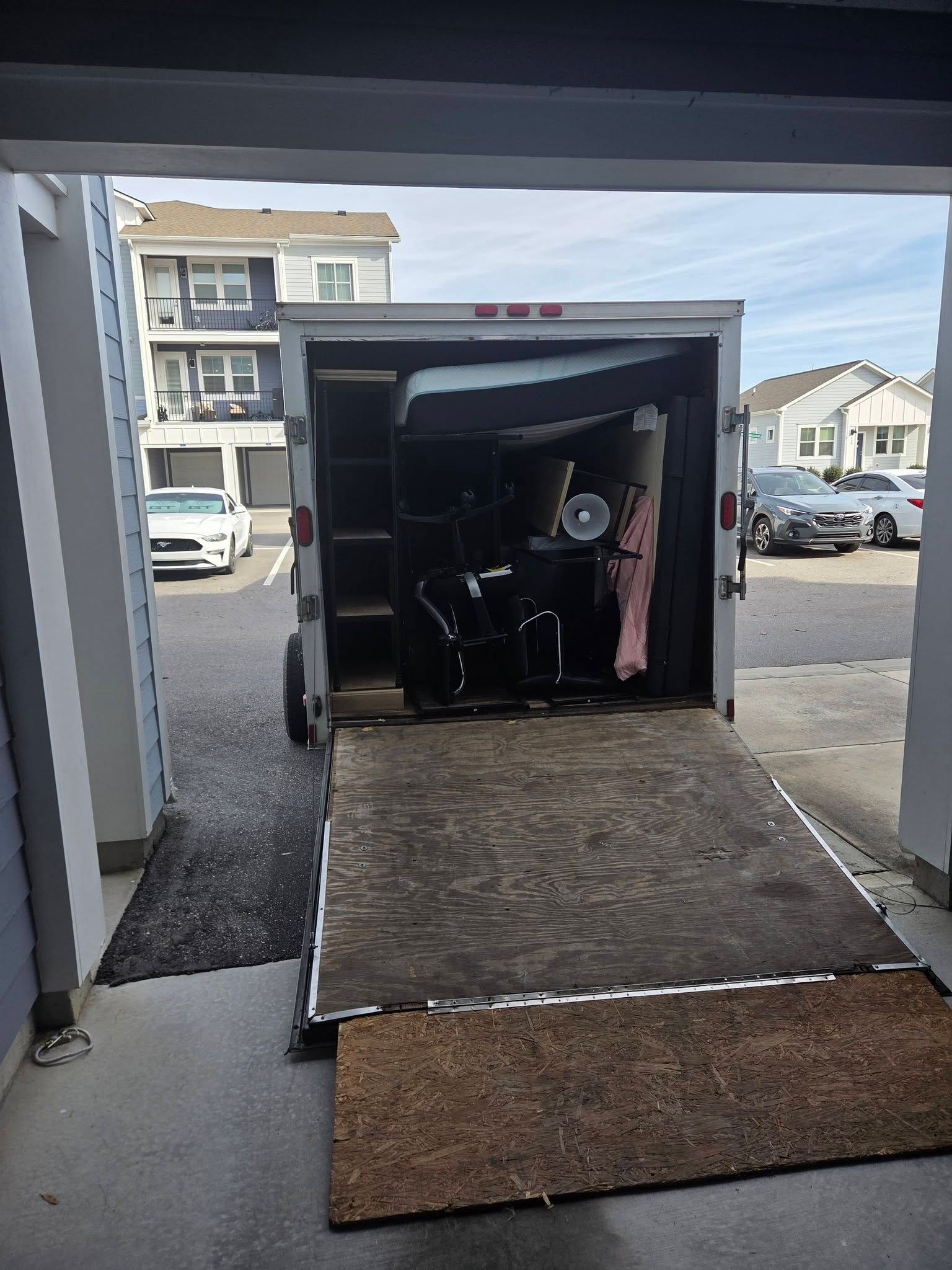 Person in wheelchair inside an enclosed trailer with a ramp, parked in a residential driveway.